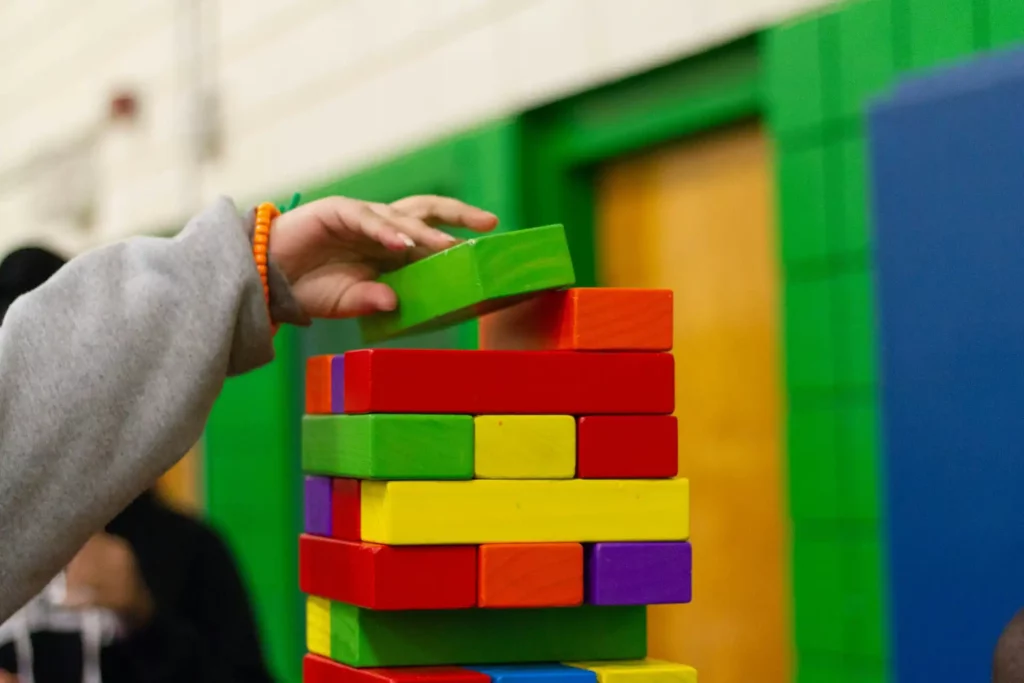 Mano di un bambino che gioca con blocchi di legno colorati, costruendo una torre in un ambiente scolastico.