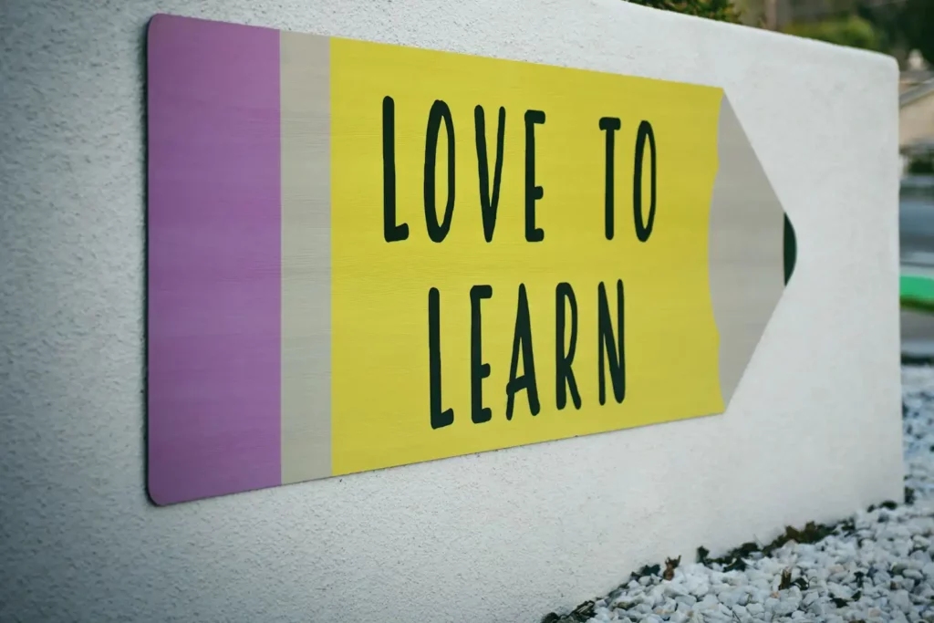 Insegna a forma di matita con la scritta "Love to Learn" su un muro bianco.